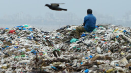 A man sits on a mountain of plastic garbage in Mumbai: India has pledged to eliminate disposable plastics within three years. (Photo by Akira Kodaka)